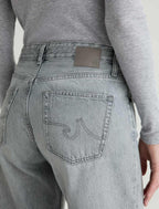 Person wearing gray jeans with a visible brand logo on the back pocket against a neutral background