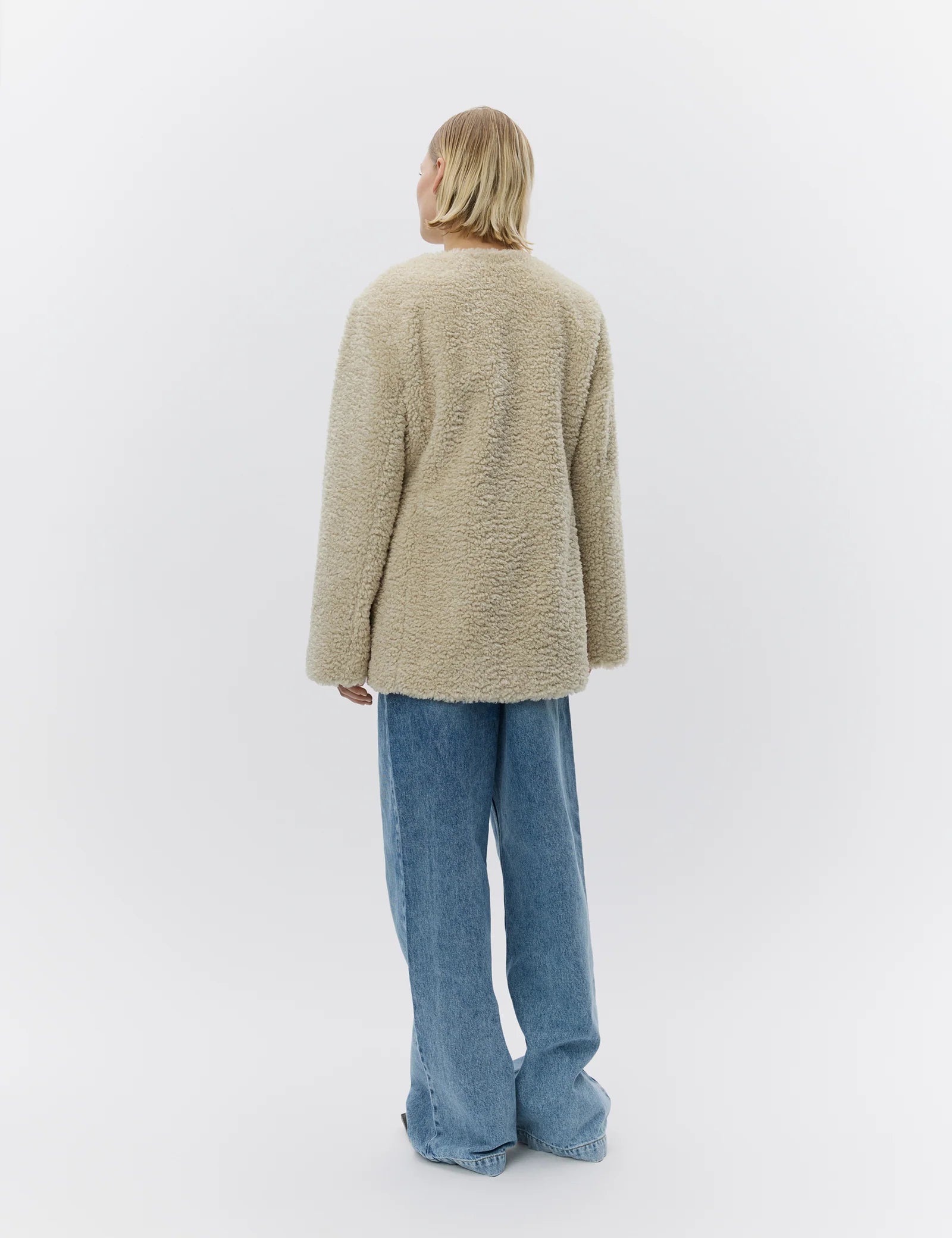 Person wearing a beige cardigan and blue jeans on a white background