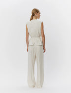 Woman wearing a light-colored sleeveless top and wide-leg pants on a white background