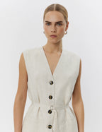 Woman wearing a sleeveless beige jumpsuit with buttons on a white background