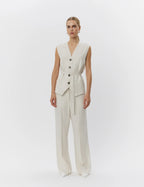 Woman wearing a beige sleeveless suit with buttons on a white background