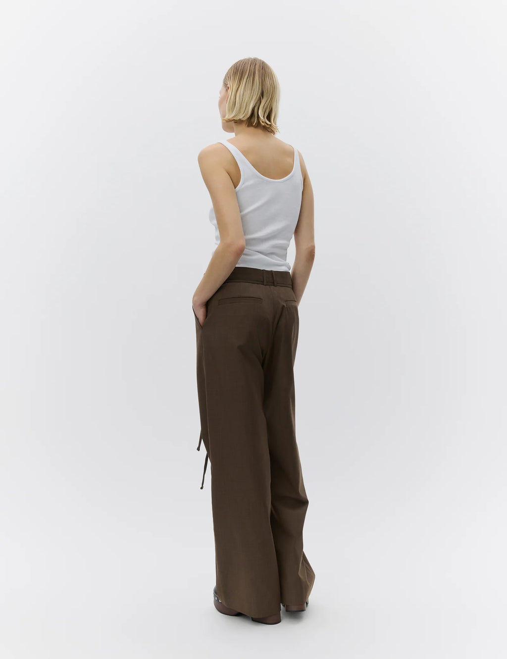 Woman wearing a white tank top and brown wide-leg pants on a white background