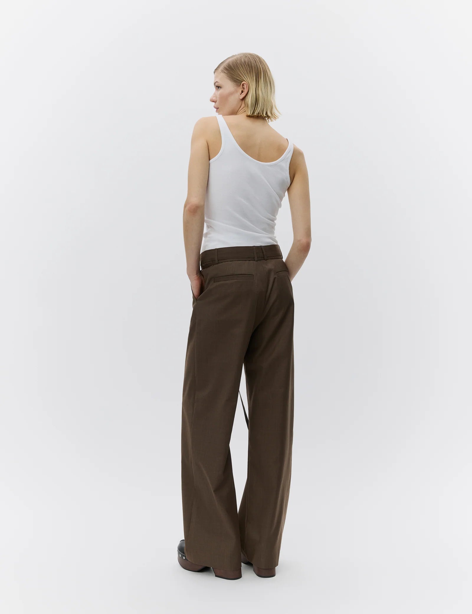 Woman wearing brown wide-leg pants and a white tank top on a white background