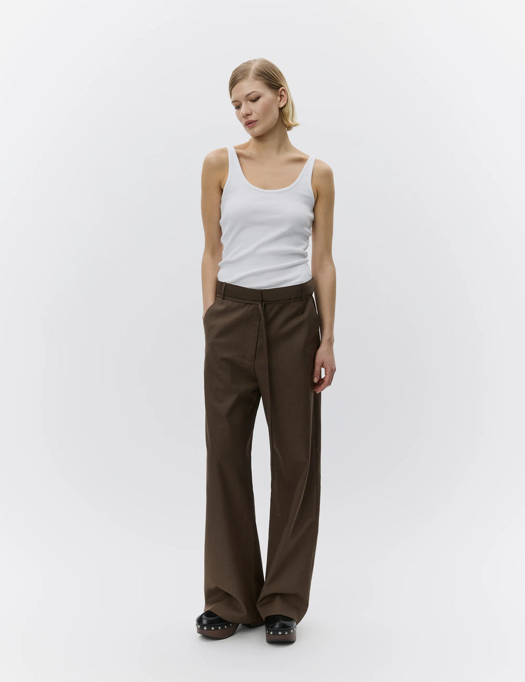 Woman wearing a white tank top and brown pants on a white background