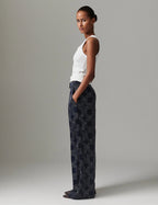 Woman wearing a white top and dark patterned pants against a gray background