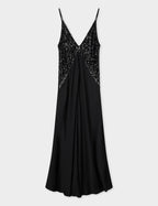 A black maxi slip dress with a deep V-neck and sequins at the chest, featuring a side zip closure and pockets. The dress has a bias-cut design and a flare in the skirt.