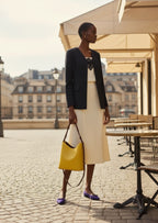 Woman holding a yellow handbag in an outdoor setting with tables and chairs.