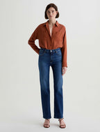 Woman wearing a rust-colored shirt and blue jeans on a white background