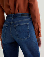 Person wearing blue jeans and a brown shirt on a plain background
