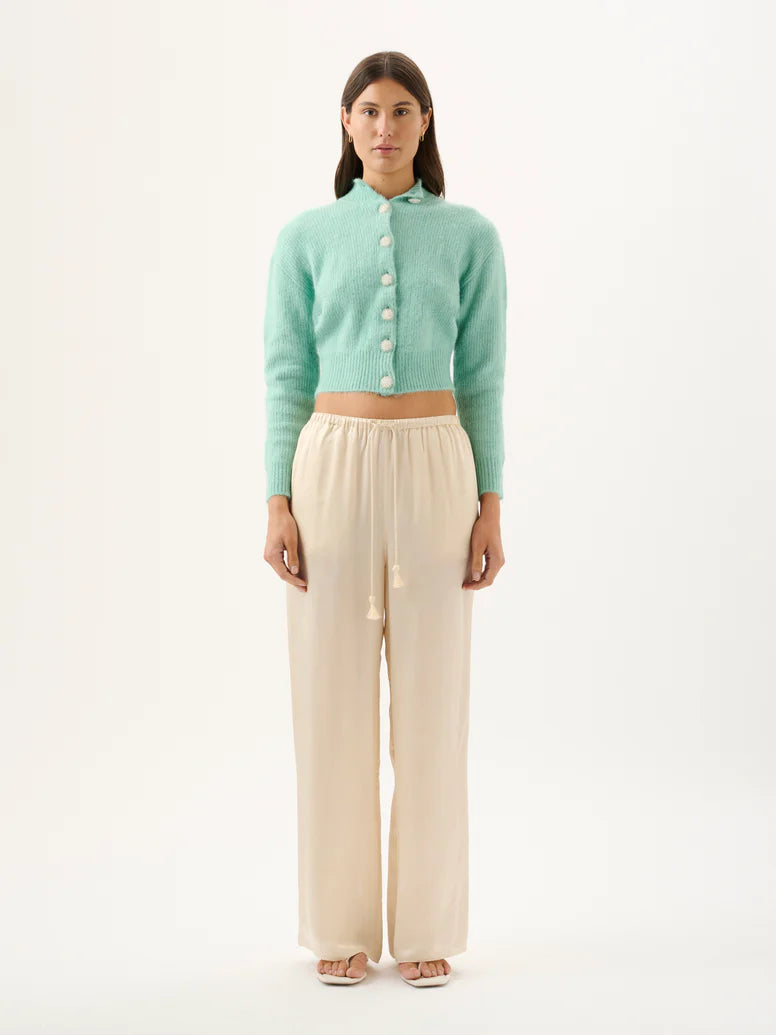 Woman wearing a light green cardigan and beige pants on a white background