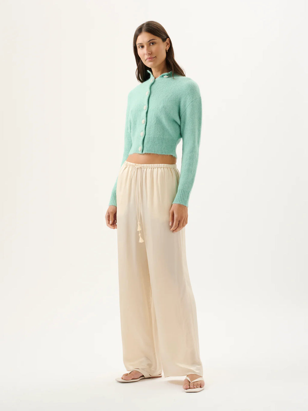 Woman wearing a light green cardigan and beige pants on a white background