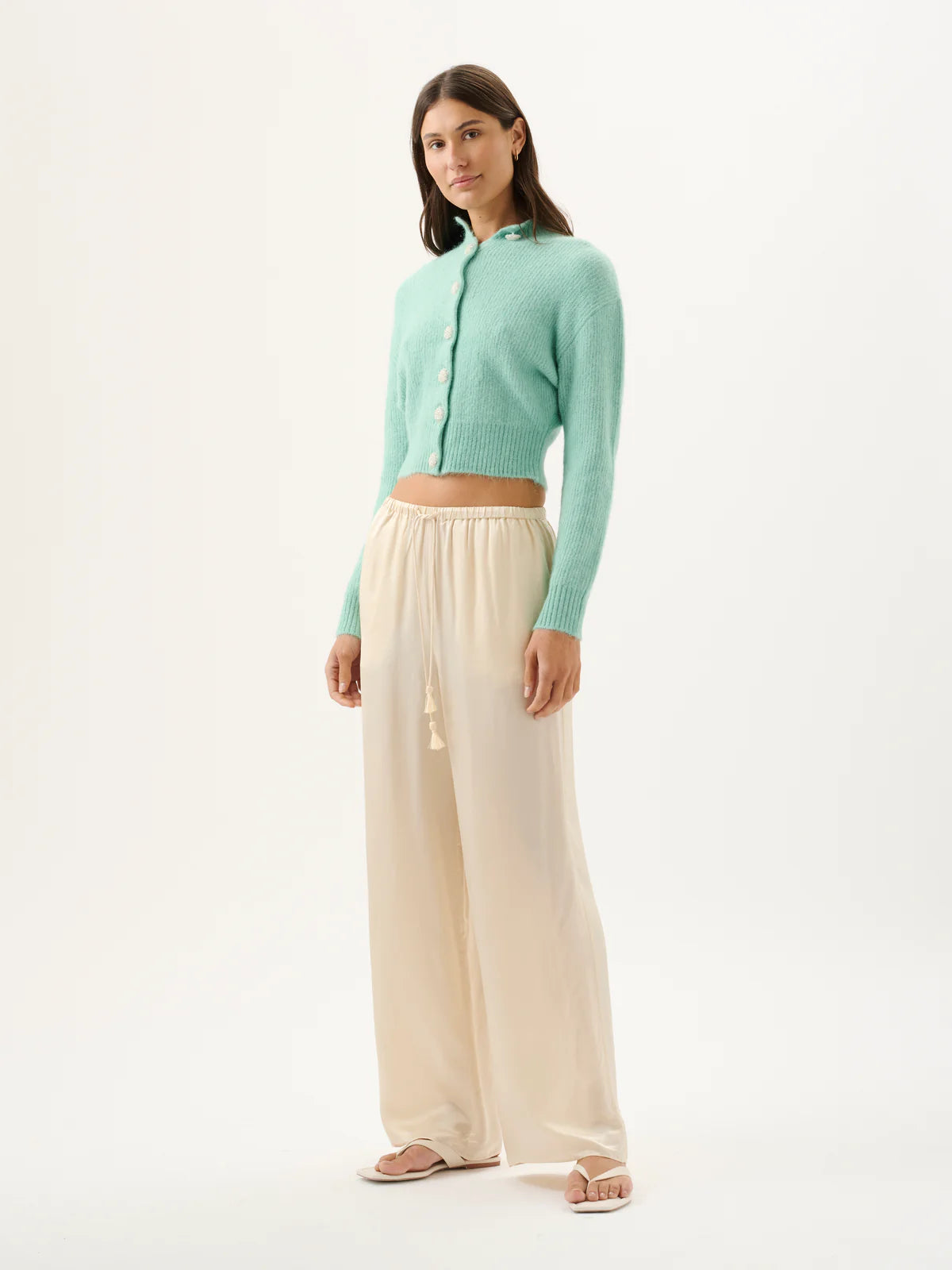 Woman wearing a light green cardigan and beige pants on a white background