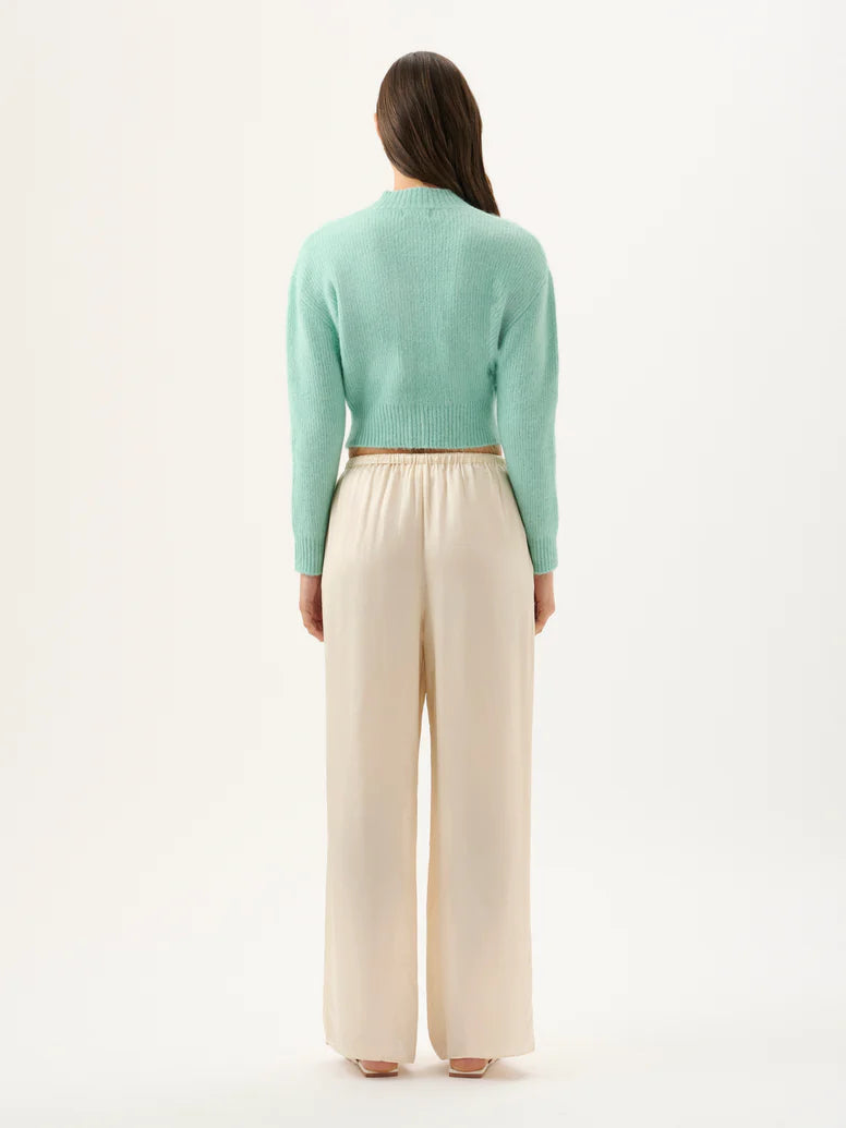 Person wearing a light green sweater and beige pants on a white background