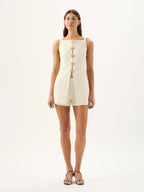 Woman wearing a cream-colored sleeveless dress with buttons on a white background