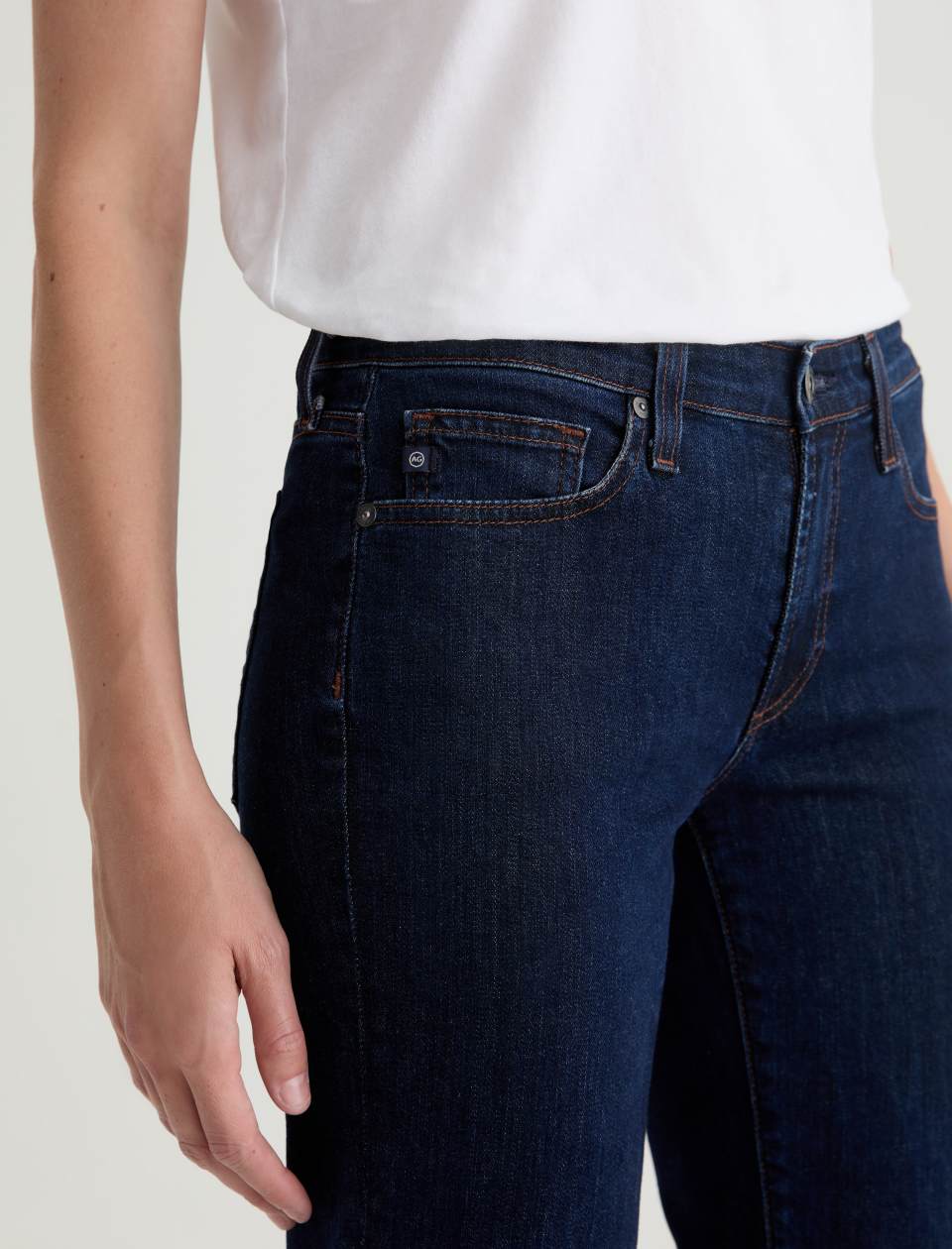Person wearing dark blue jeans and a white shirt on a light background