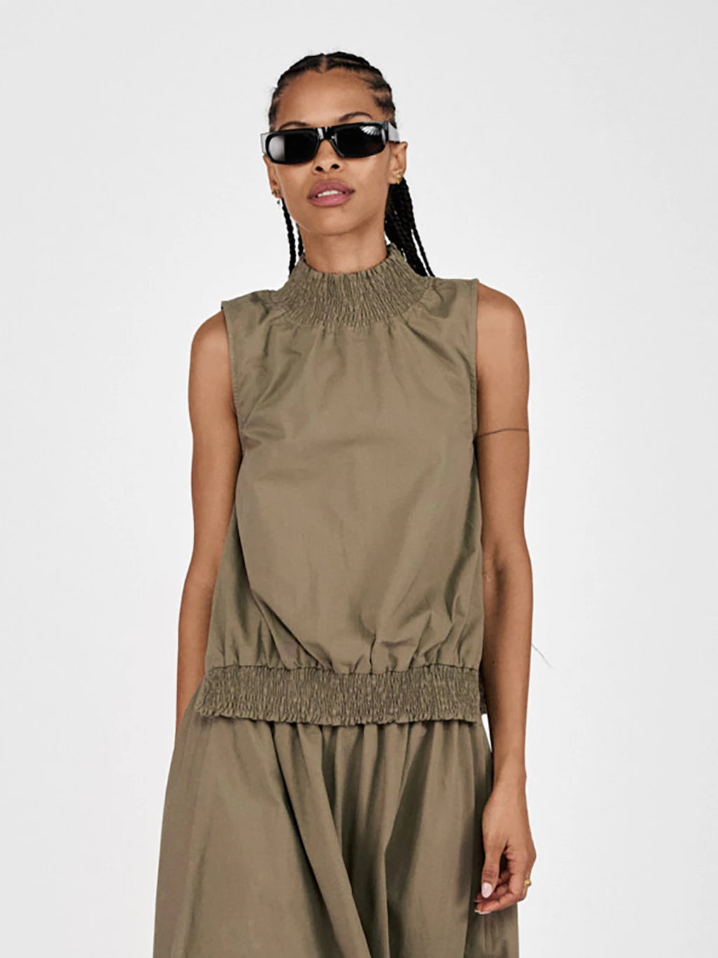 Woman wearing a sleeveless olive green dress with a plain background