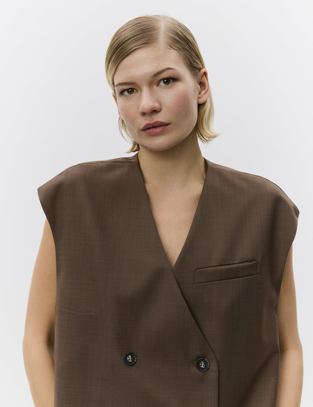 Woman wearing a brown sleeveless blazer against a plain background