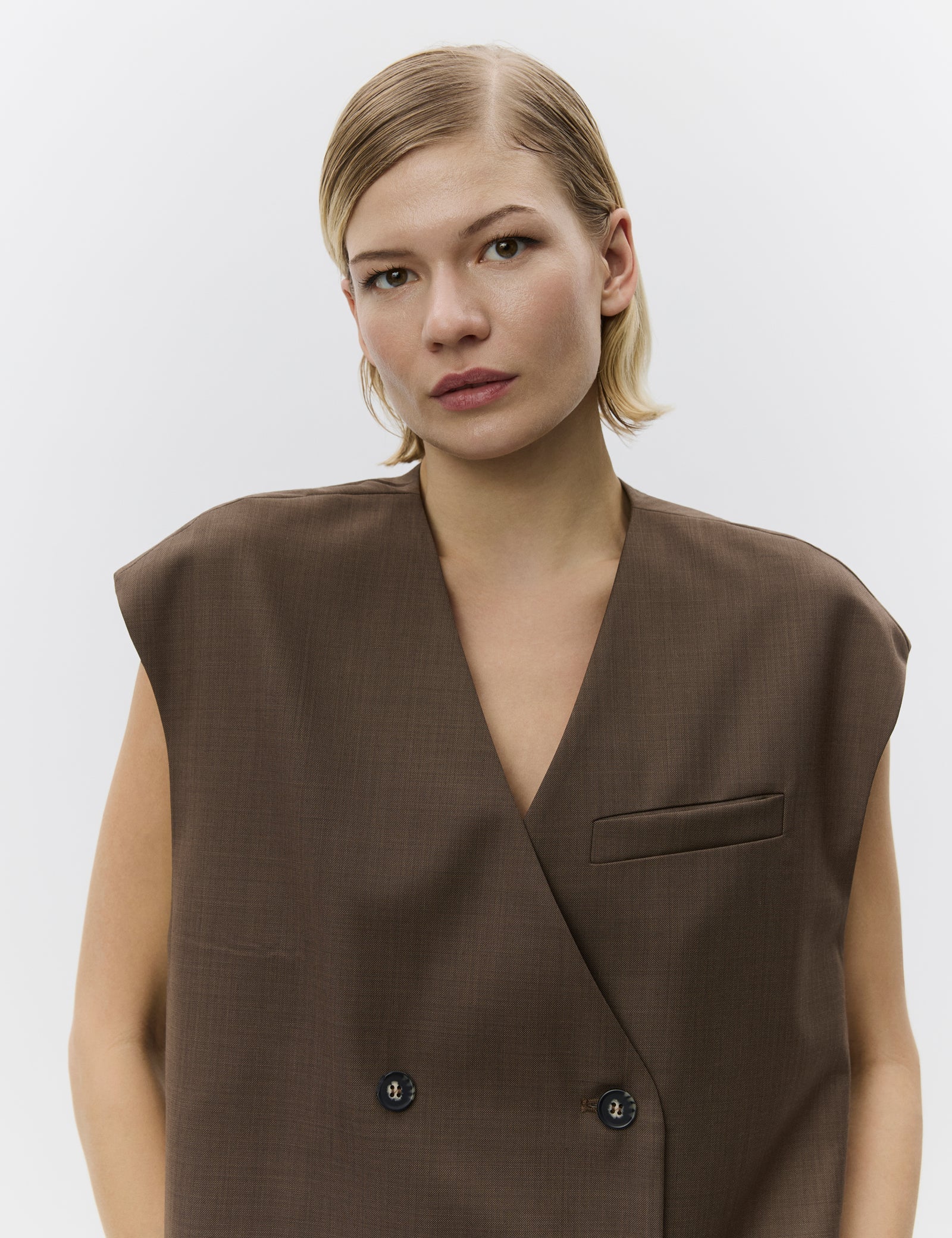 Woman wearing a brown sleeveless blazer against a plain background