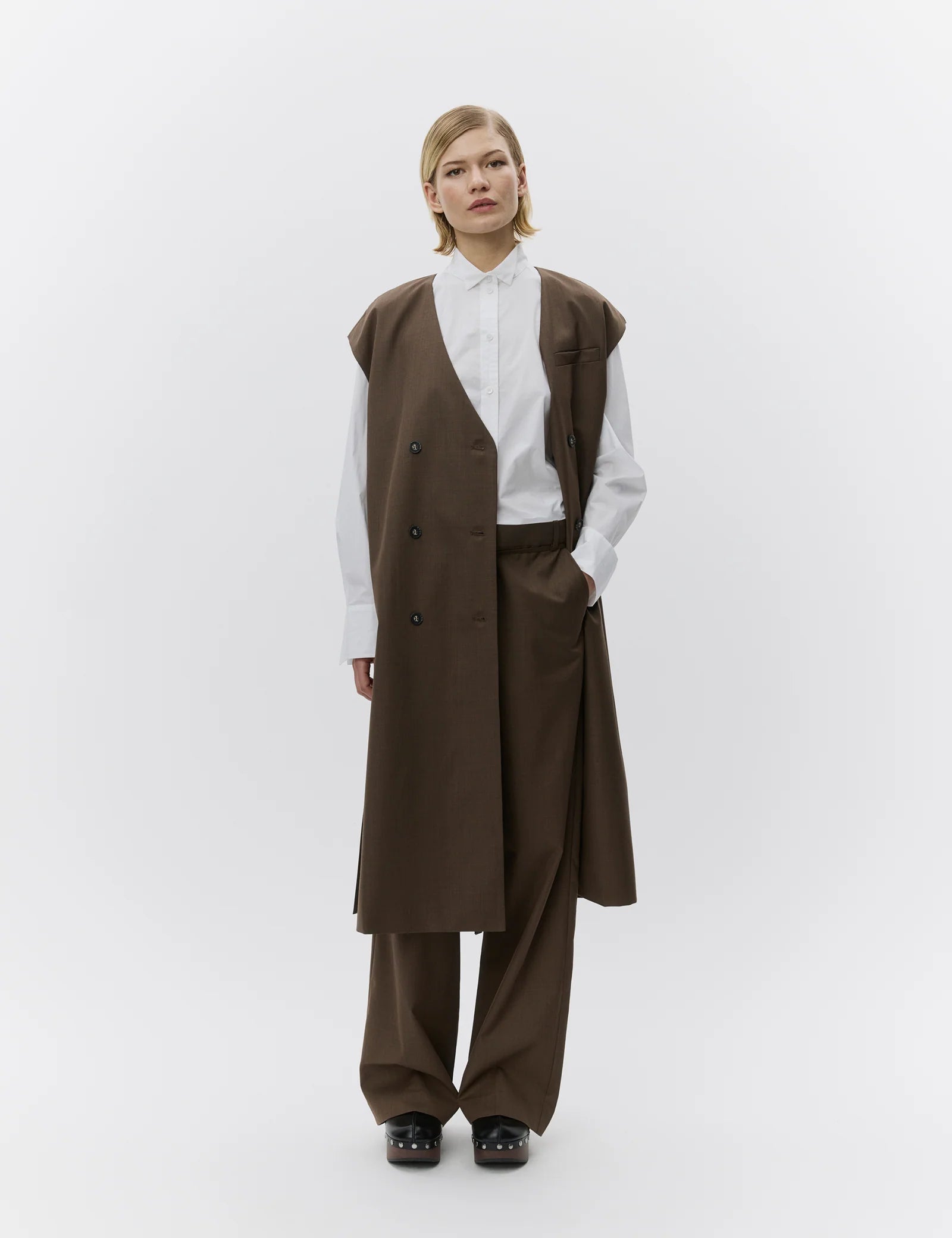 Person wearing a brown vest and pants with a white shirt on a white background