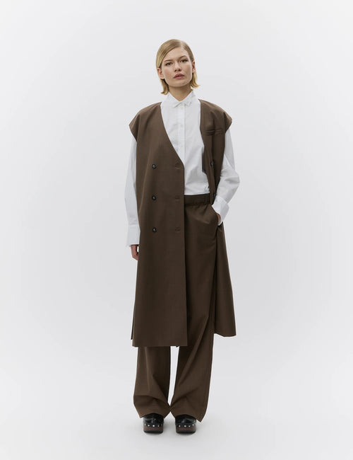 Person wearing a brown vest and pants with a white shirt on a white background