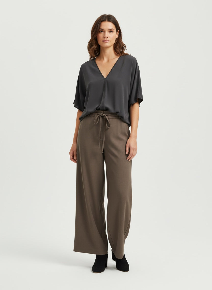 Woman wearing a dark gray blouse and brown wide-leg pants on a white background