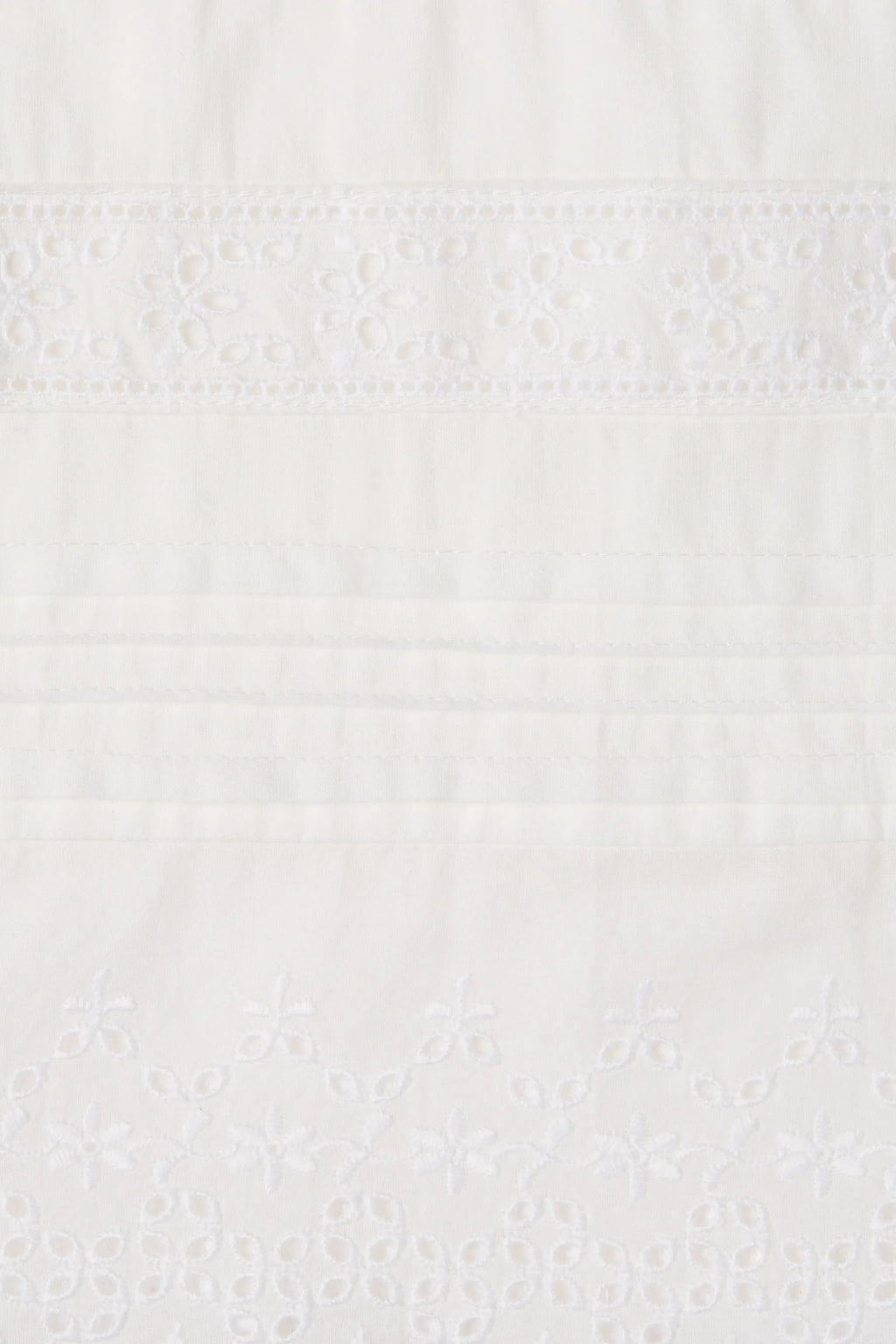 Close-up of a white embroidered fabric with delicate floral eyelet embroidery and horizontal stitched bands.