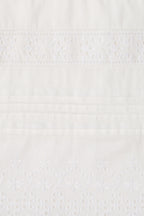 Close-up of a white embroidered fabric with delicate floral eyelet embroidery and horizontal stitched bands.