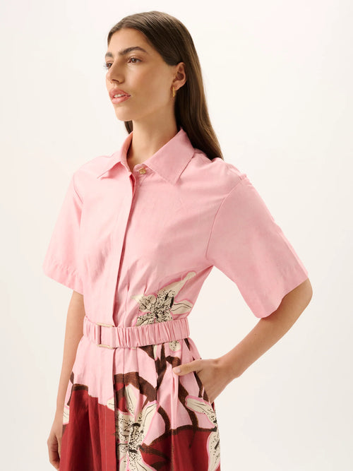 Woman wearing a pink shirt with a belt and red patterned skirt on a white background