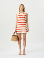 Woman wearing a red and white striped dress holding a woven bag on a white background