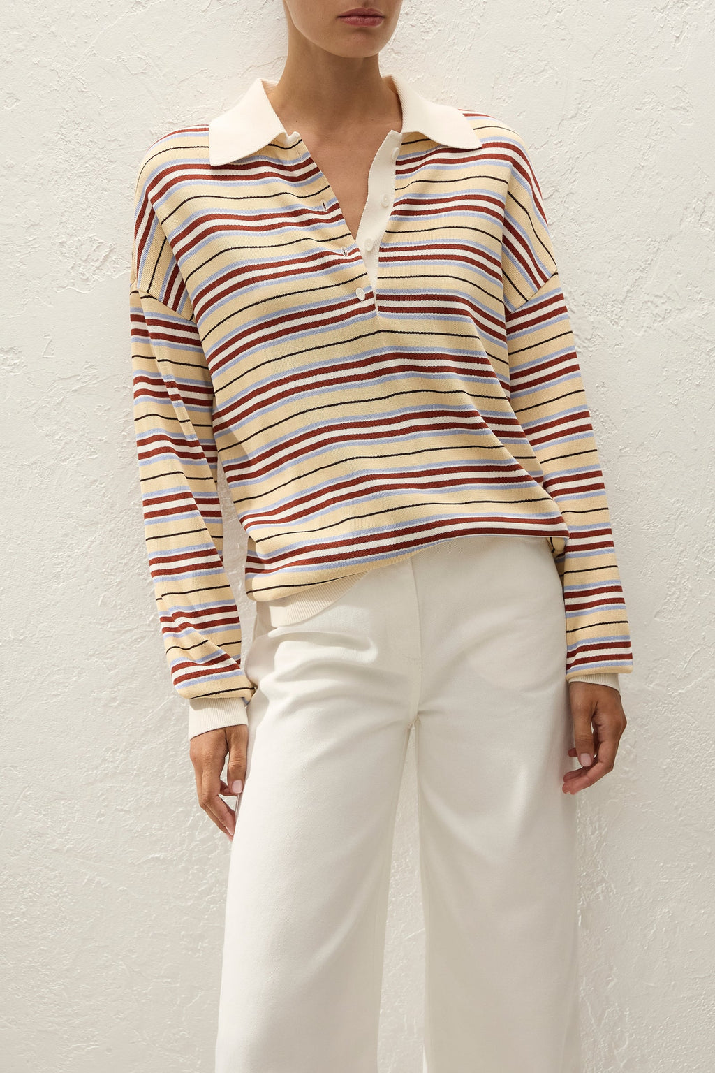 Person wearing a striped long-sleeve shirt and white pants against a light background