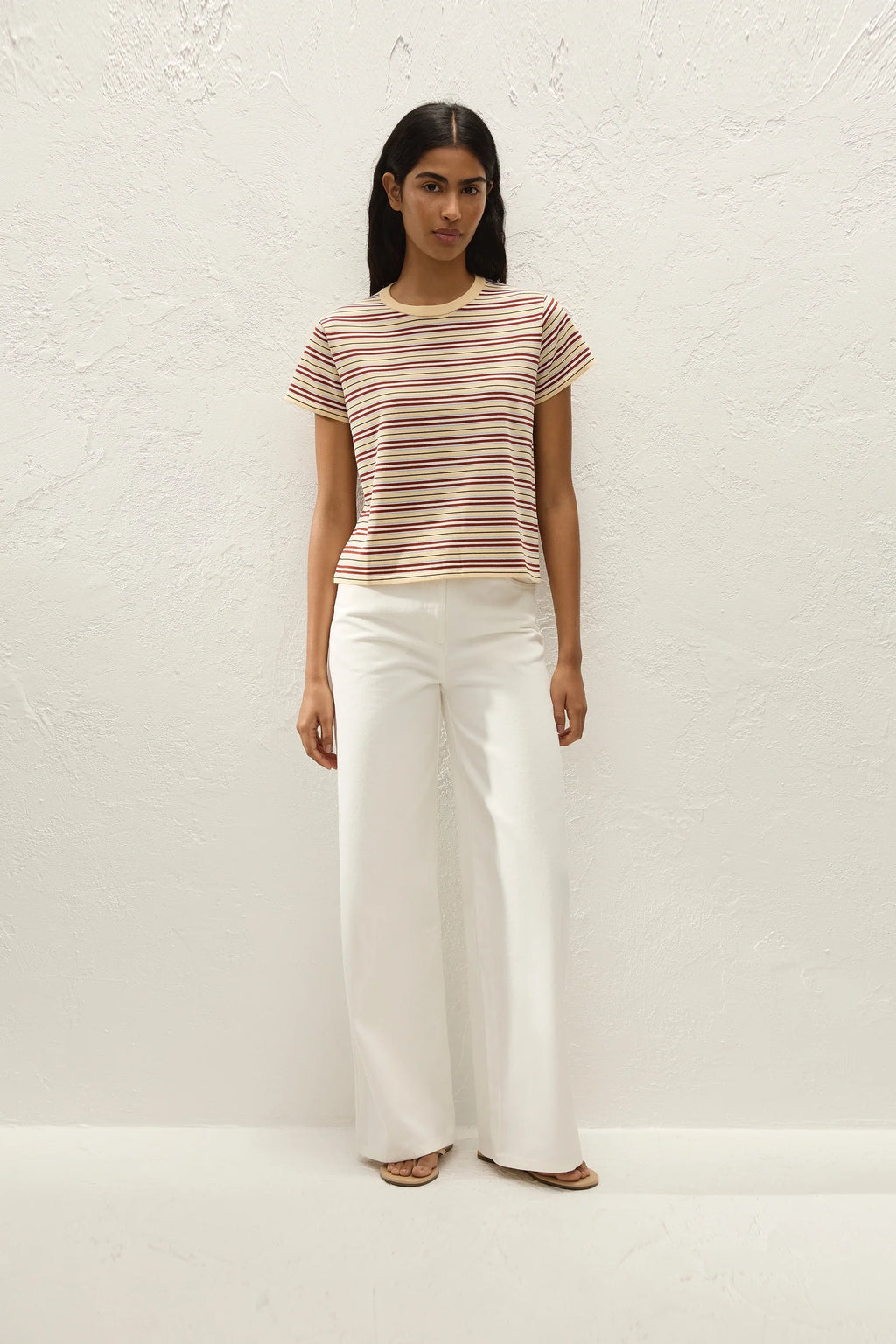 Woman wearing a striped shirt and white pants against a white background