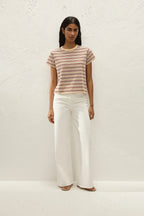 Woman wearing a striped shirt and white pants against a white background