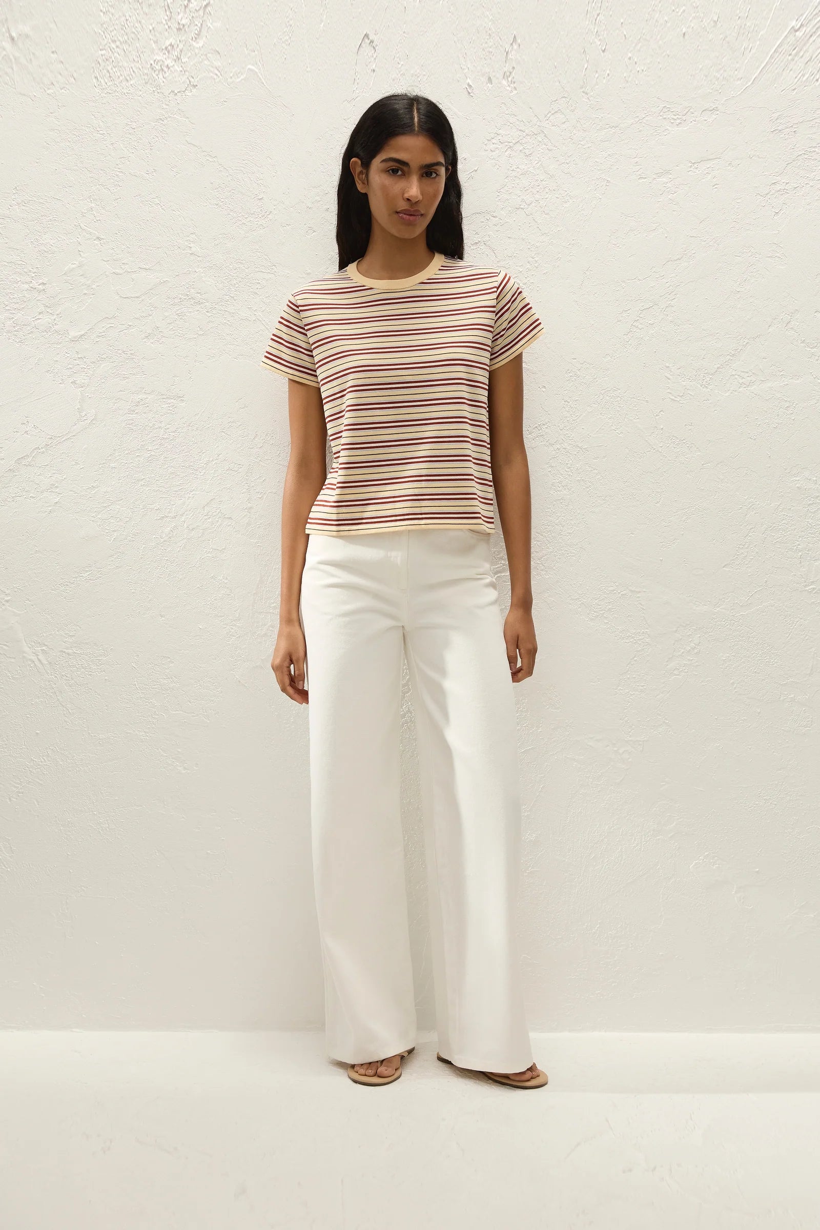 Woman wearing a striped shirt and white pants against a white background