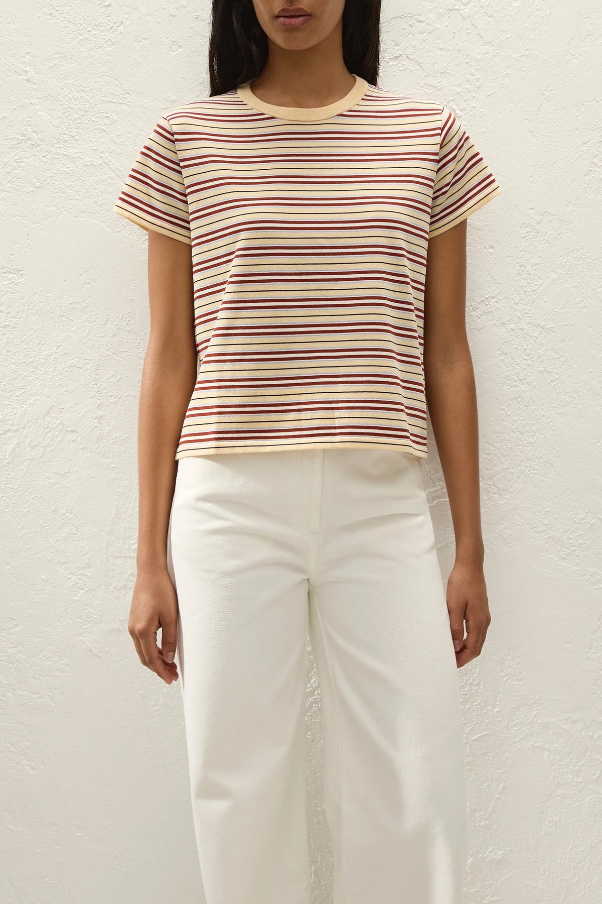 Person wearing a striped shirt and white pants against a plain background