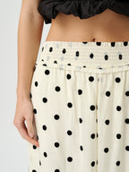 Close-up of a person wearing cream-colored wide-leg pants with black polka dots and a smocked elastic waistband, paired with a black ruffled top.
