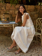 Woman in a white dress sitting outdoors near a stone wall.