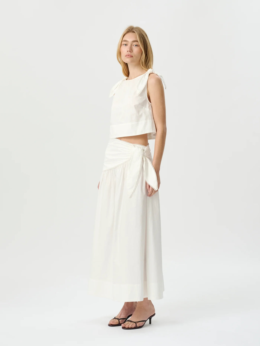 Woman wearing a white sleeveless top and wide-leg pants on a white background