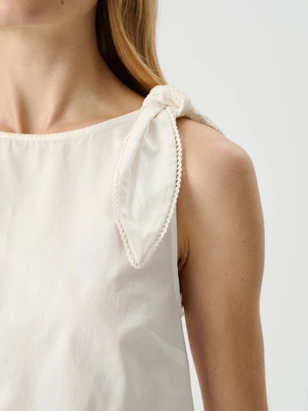 White sleeveless top with tied shoulder straps on a neutral background