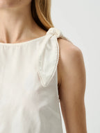 White sleeveless top with tied shoulder straps on a neutral background