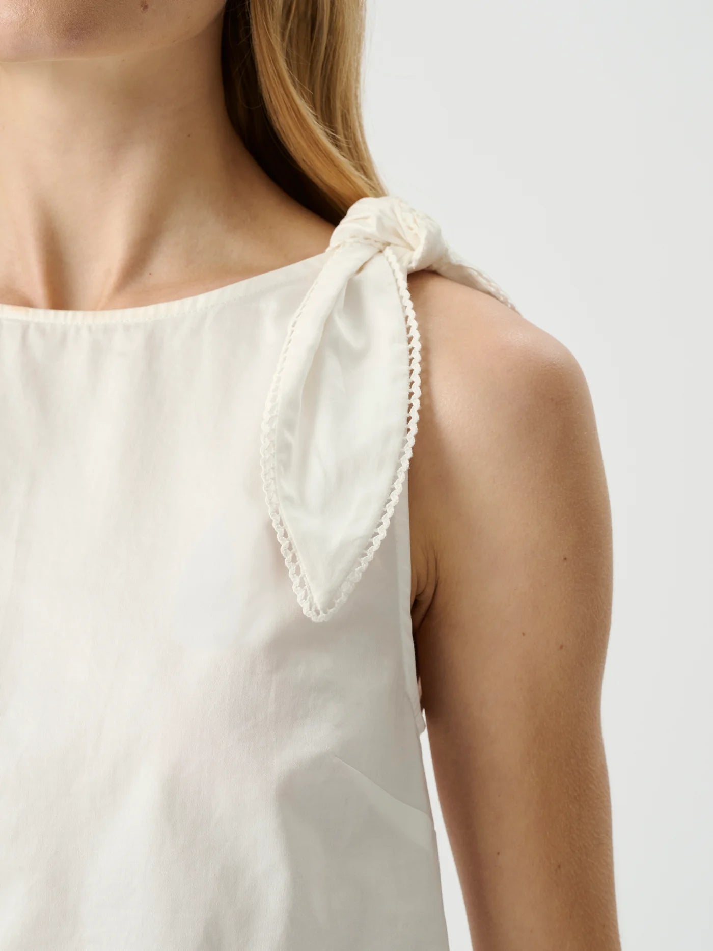 White sleeveless top with tied shoulder straps on a neutral background