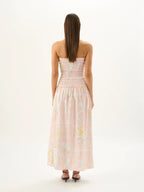 Woman wearing a strapless pink dress with floral pattern on a white background