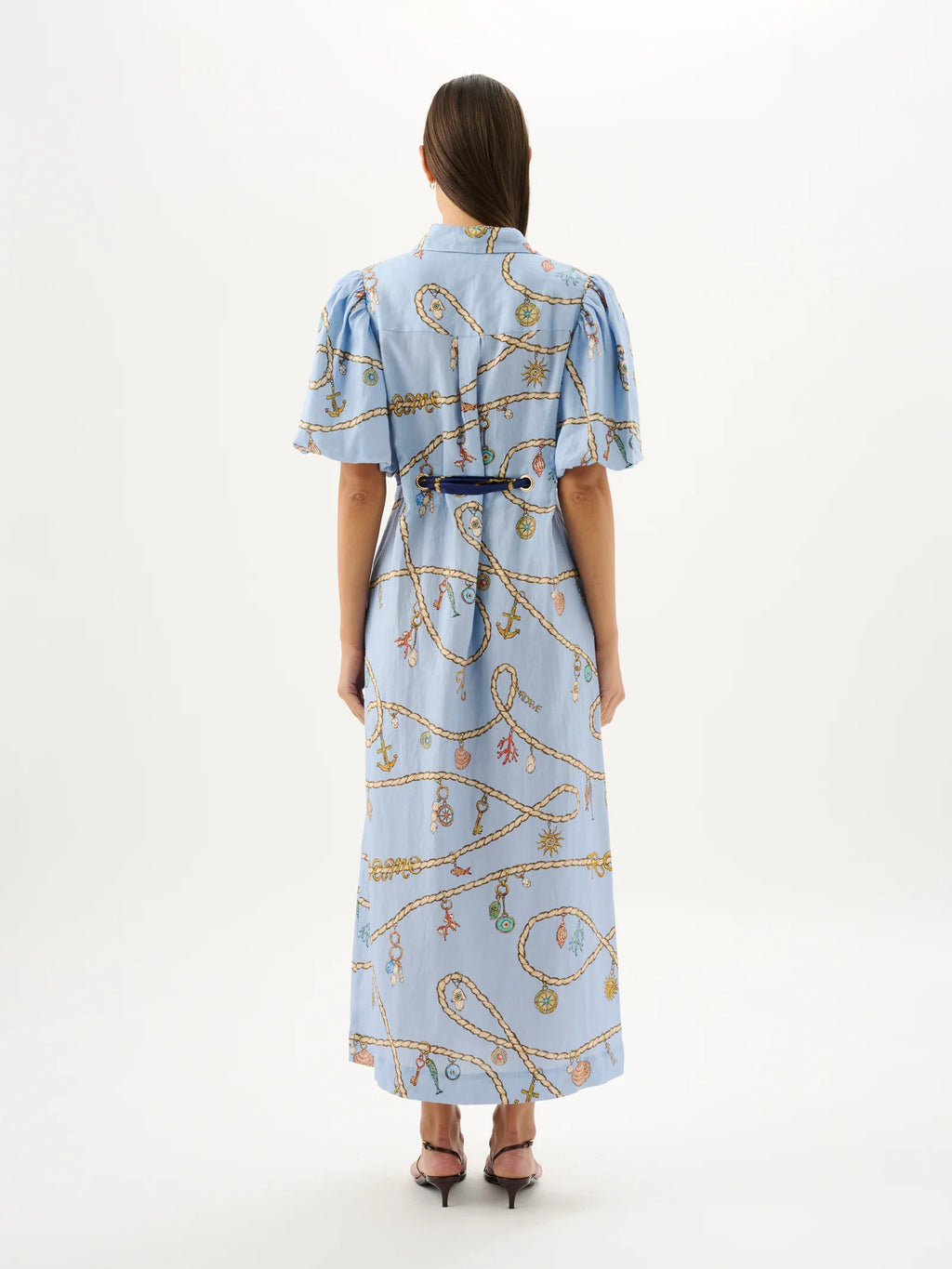 Woman wearing a light blue dress with a pattern, standing against a white background