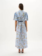 Woman wearing a light blue dress with a pattern, standing against a white background