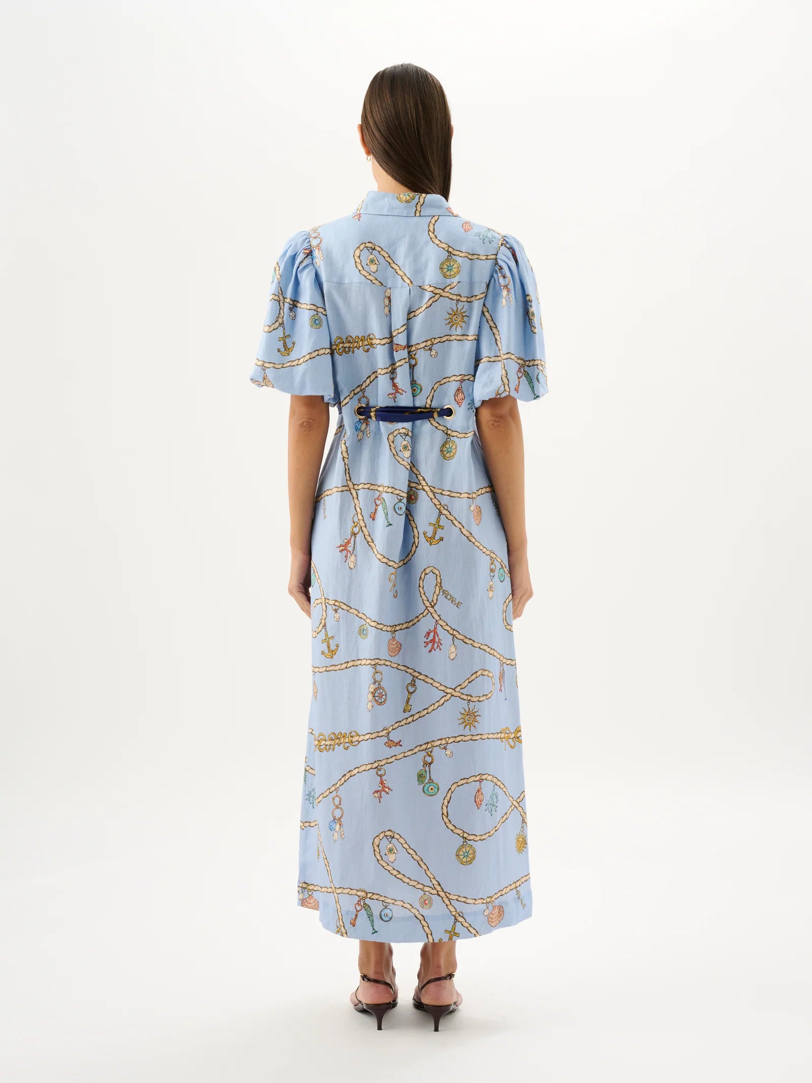 Woman wearing a light blue dress with a pattern, standing against a white background