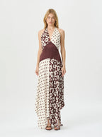 A model wearing a sleeveless halter-neck maxi dress with a mixed print design of brown polka dots, floral patterns, and a solid dark brown waist panel, set against a plain white studio background.