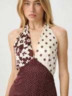 A woman wearing a halter-neck dress with a split design: one side has a cream background with dark brown floral print, and the other side and lower portion have a dark brown background with small cream polka dots.