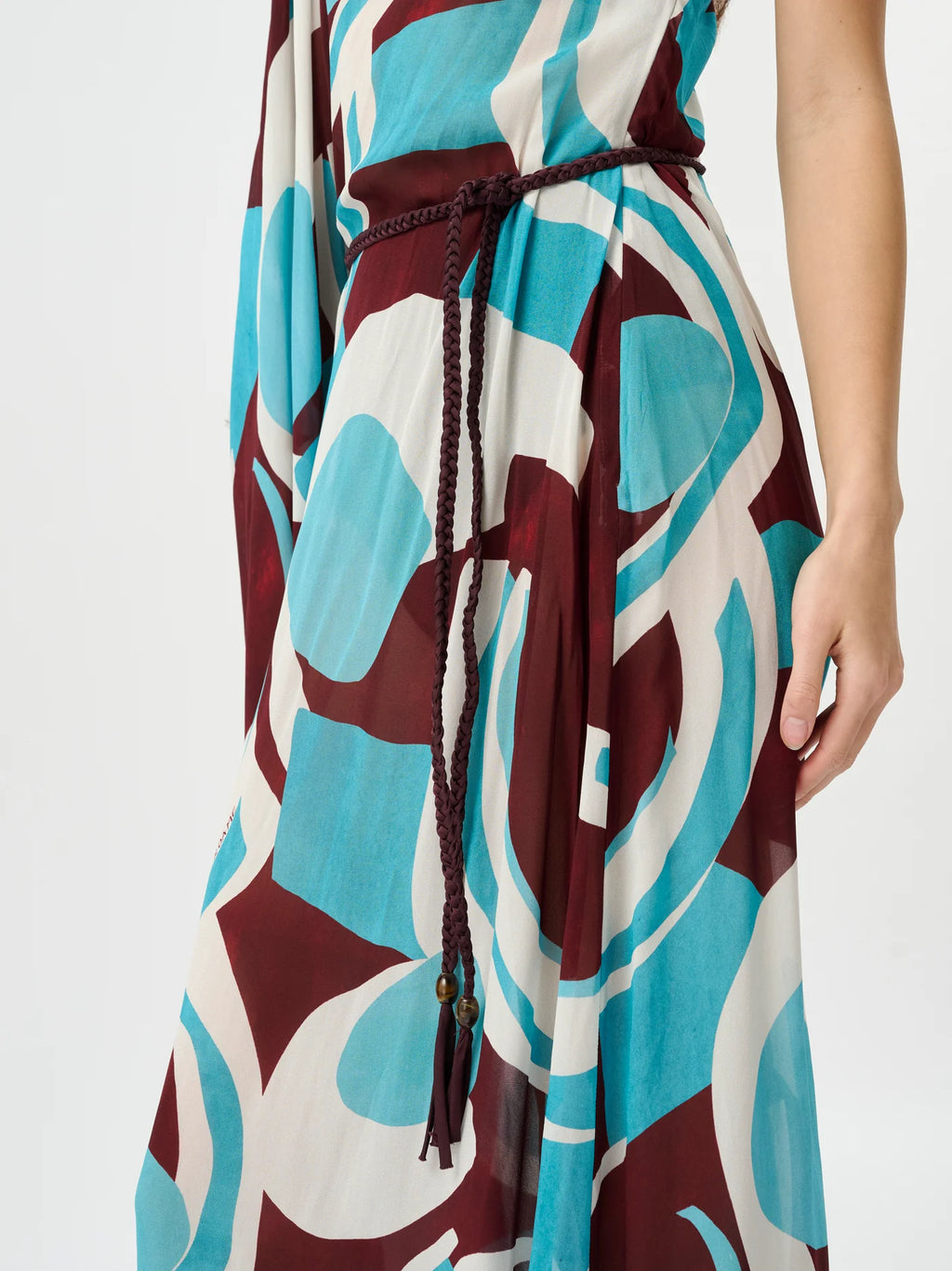 A close-up of a sleeveless dress with an abstract geometric pattern in teal, burgundy, and off-white, featuring a dark brown braided tie belt at the waist.
