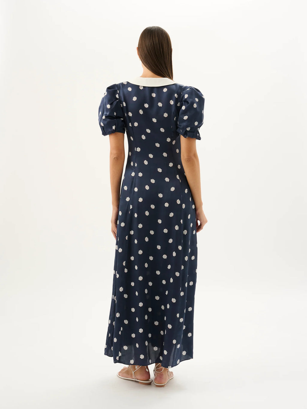 Woman wearing a navy dress with white polka dots from behind on a white background