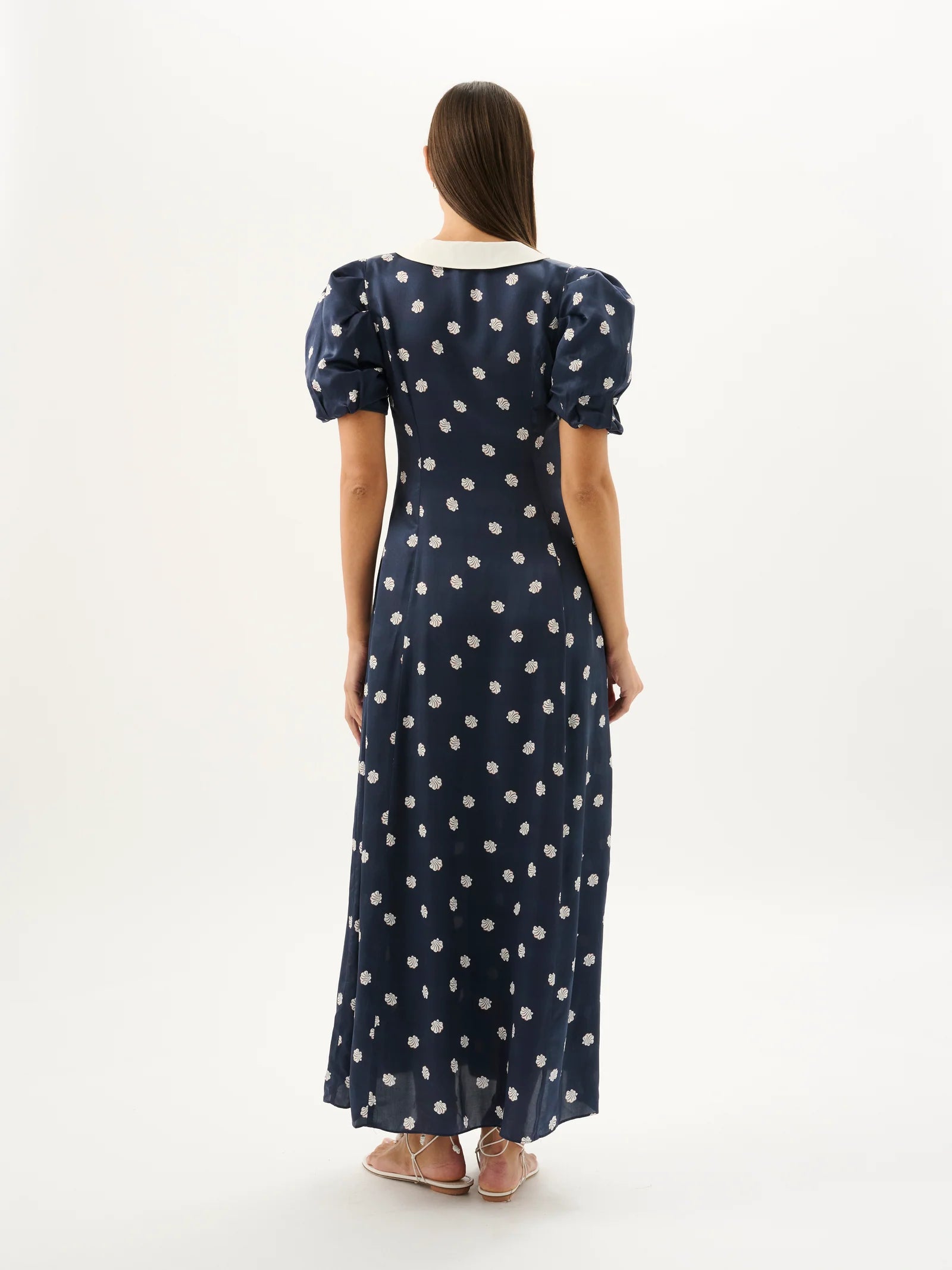 Woman wearing a navy dress with white polka dots from behind on a white background