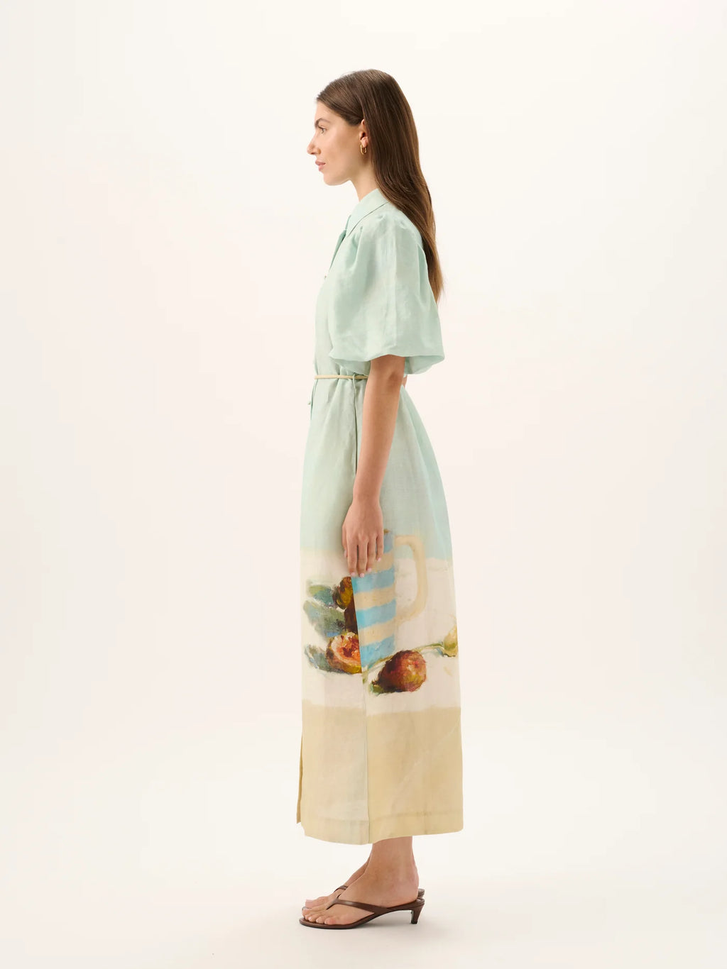 Woman wearing a light green dress with a scenic print on a white background